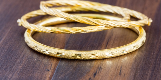 Three gold bracelets lying on a wooden table